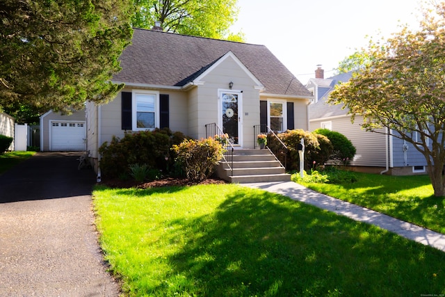 view of front of home featuring asphalt driveway, a front yard, roof with shingles, and an outdoor structure