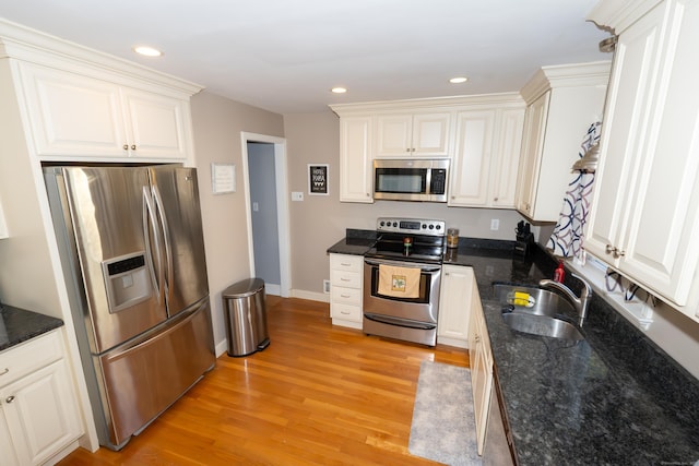 kitchen featuring appliances with stainless steel finishes, a sink, light wood-style floors, white cabinetry, and recessed lighting