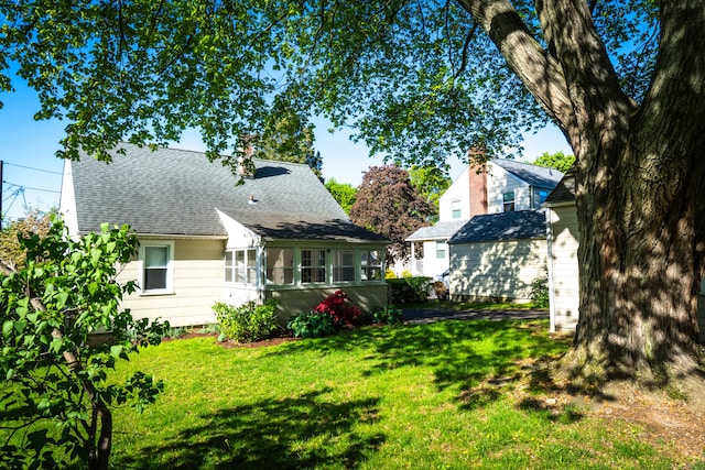 rear view of house featuring roof with shingles and a yard