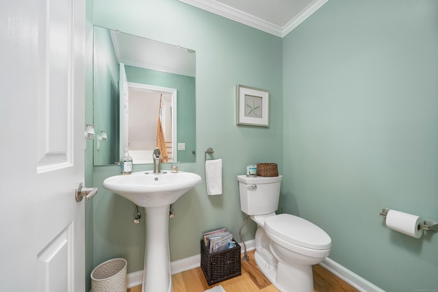 bathroom featuring wood finished floors, toilet, ornamental molding, a sink, and baseboards