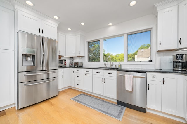 kitchen featuring stainless steel appliances, a sink, light wood finished floors, decorative backsplash, and recessed lighting