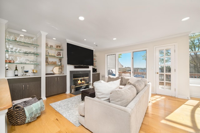 living area with ornamental molding, light wood-type flooring, recessed lighting, and a fireplace with flush hearth