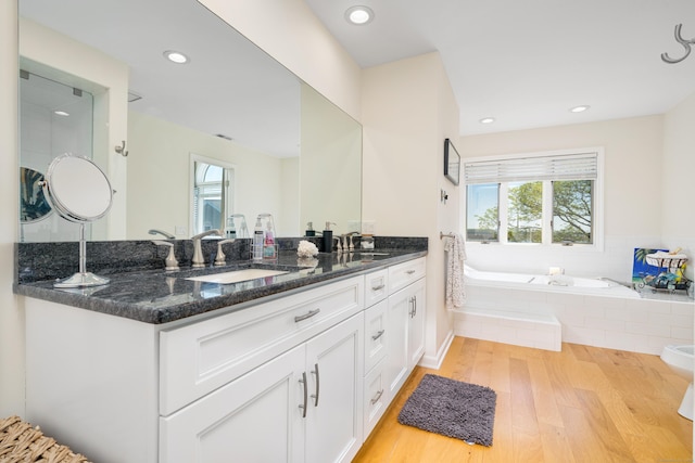 full bath with wood finished floors, a bath, double vanity, and recessed lighting