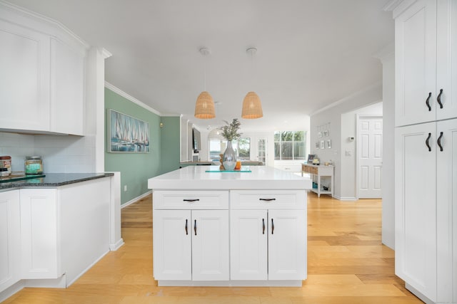 kitchen featuring baseboards, white cabinets, light wood-type flooring, decorative backsplash, and ornamental molding