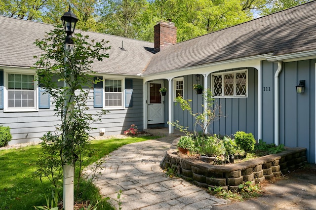 doorway to property with board and batten siding, a chimney, and roof with shingles