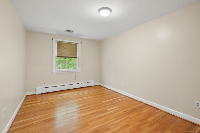 empty room featuring a baseboard radiator, baseboards, and light wood-style flooring