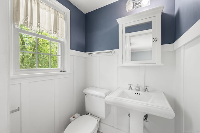 half bath with toilet, a sink, a decorative wall, and a wainscoted wall