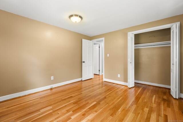 unfurnished bedroom featuring light wood-style flooring, baseboards, and a closet