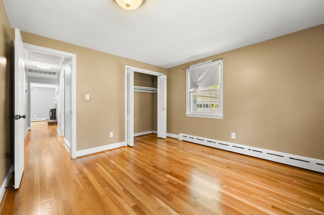 unfurnished bedroom with attic access, light wood-type flooring, a baseboard heating unit, a closet, and baseboards