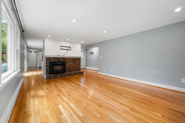 unfurnished living room with a baseboard heating unit, baseboards, light wood finished floors, a fireplace, and recessed lighting