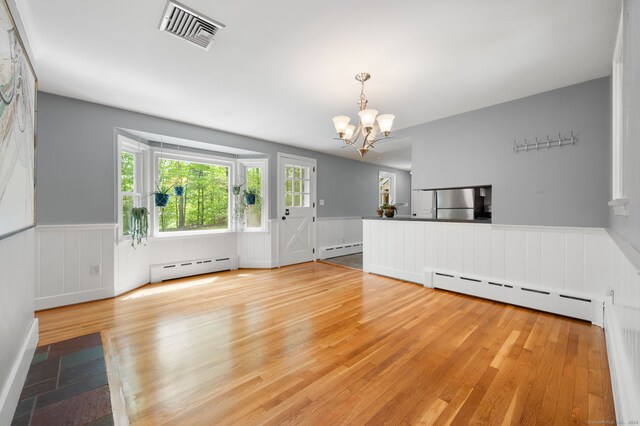 unfurnished living room with a baseboard radiator, a chandelier, a wainscoted wall, and wood finished floors
