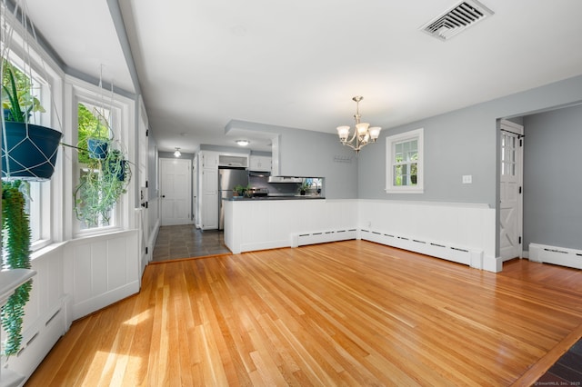unfurnished living room featuring a baseboard heating unit, a chandelier, and light wood finished floors