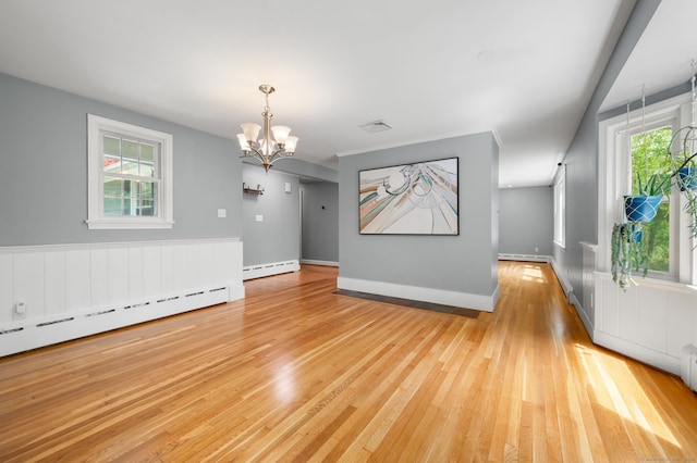 spare room with a chandelier, a baseboard heating unit, light wood-style floors, and plenty of natural light