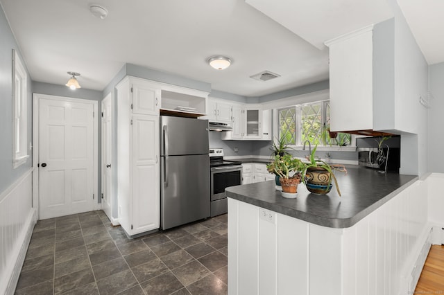 kitchen featuring appliances with stainless steel finishes, a peninsula, dark countertops, under cabinet range hood, and white cabinetry
