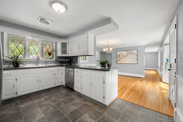 kitchen featuring appliances with stainless steel finishes, dark countertops, a peninsula, a sink, and white cabinets