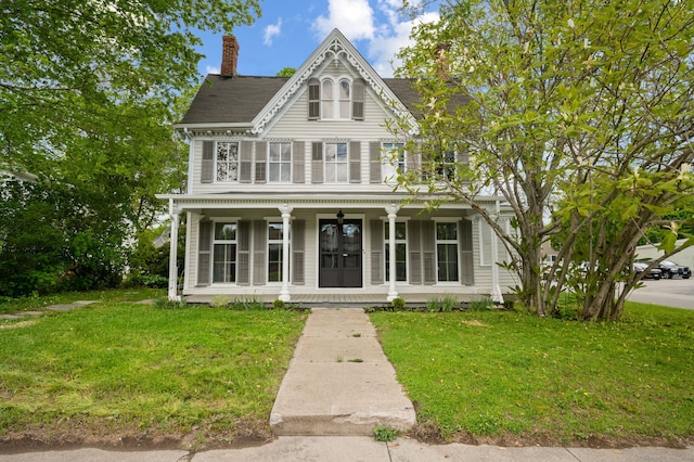 victorian home featuring covered porch, a chimney, and a front yard