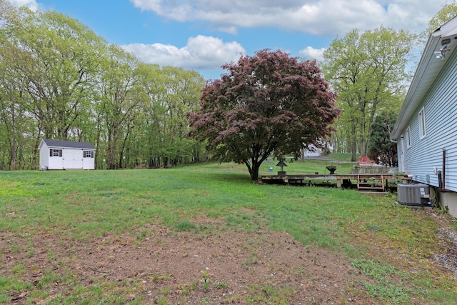 view of green lawn with an outdoor structure, a wooden deck, and central air condition unit