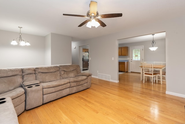 living area with light wood-type flooring, a ceiling fan, baseboards, and a chandelier