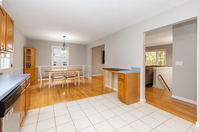 kitchen with stainless steel dishwasher, light wood-style floors, brown cabinets, and hanging light fixtures
