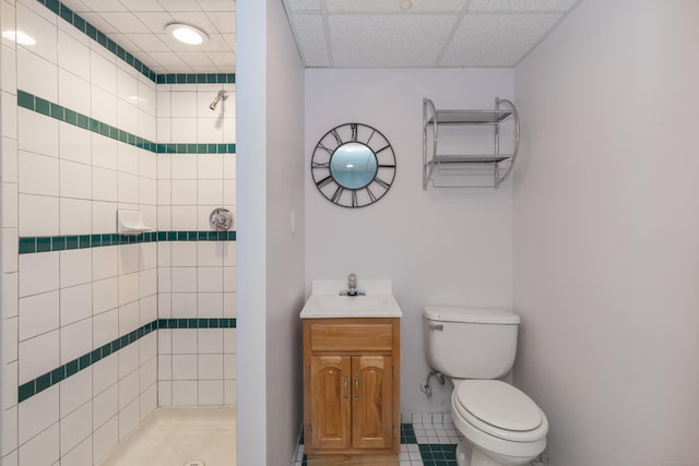 bathroom featuring tiled shower, toilet, vanity, a paneled ceiling, and tile patterned flooring