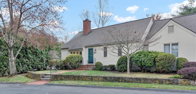 cape cod house featuring a chimney, a shingled roof, and a front yard