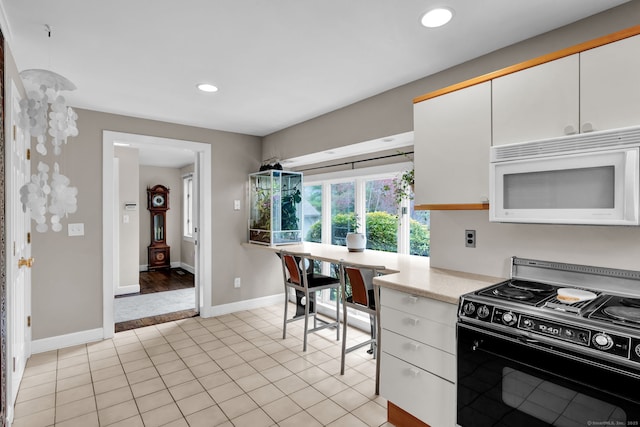 kitchen with white microwave, black range with electric stovetop, light countertops, baseboards, and white cabinetry