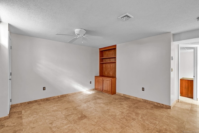 unfurnished room featuring a textured ceiling, a ceiling fan, built in features, and baseboards