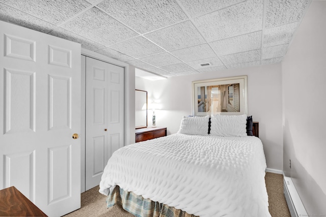 bedroom featuring carpet, a baseboard radiator, a closet, baseboards, and a drop ceiling
