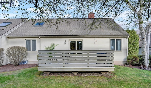 rear view of property with a wooden deck, roof with shingles, a chimney, and a lawn