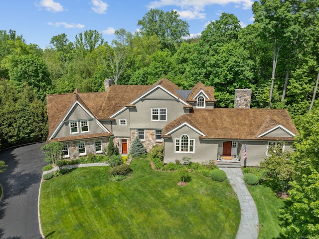 shingle-style home with a chimney, a front yard, and stone siding