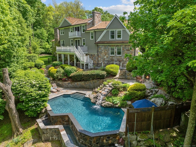 rear view of house featuring stairs, stone siding, a chimney, an outdoor pool, and fence