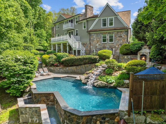 back of house featuring stairs, stone siding, an outdoor stone fireplace, and an outdoor pool