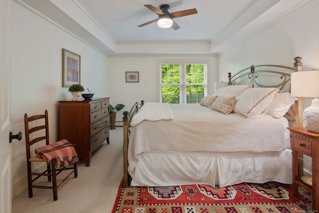 carpeted bedroom with a raised ceiling, ornamental molding, and a ceiling fan