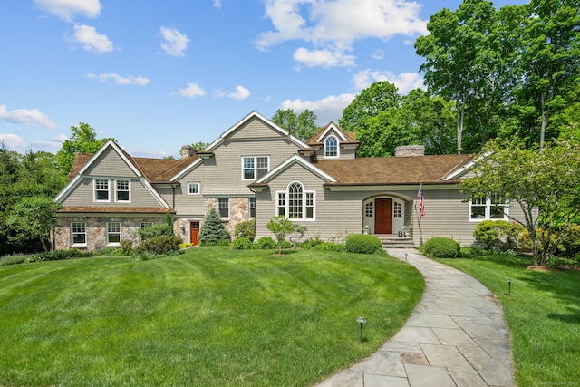 shingle-style home featuring a chimney, a front lawn, and stone siding