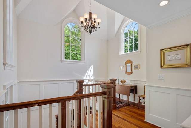 hall featuring healthy amount of natural light, a decorative wall, a wainscoted wall, vaulted ceiling, and a chandelier