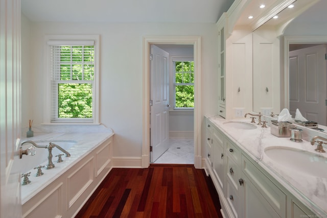 bathroom with baseboards, wood finished floors, a bath, and double vanity
