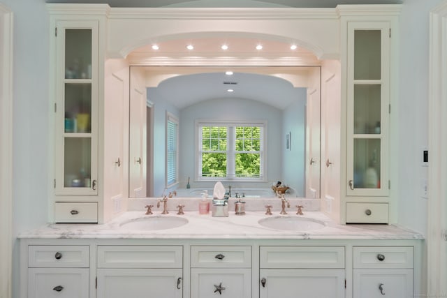bathroom featuring a bath, double vanity, lofted ceiling, and recessed lighting