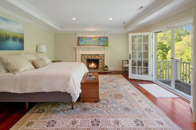 bedroom with wood finished floors, a tray ceiling, crown molding, access to outside, and a fireplace