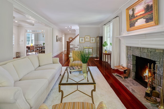 living area featuring stairway, dark wood-type flooring, crown molding, a stone fireplace, and ceiling fan