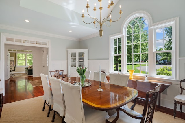 dining space with wood finished floors, a decorative wall, ornamental molding, a wainscoted wall, and a chandelier