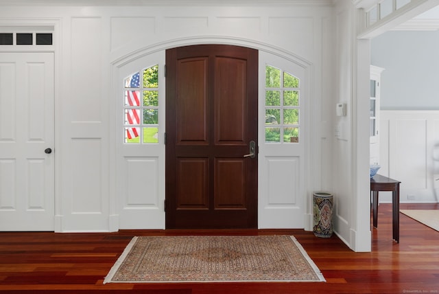 entrance foyer with a decorative wall, plenty of natural light, dark wood finished floors, arched walkways, and wainscoting