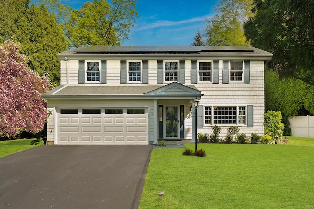colonial home with asphalt driveway, a front yard, a garage, and roof mounted solar panels