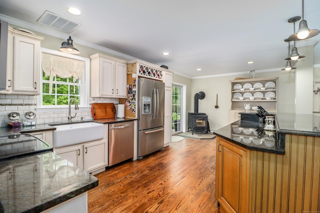 kitchen featuring appliances with stainless steel finishes, a sink, crown molding, a wood stove, and healthy amount of natural light
