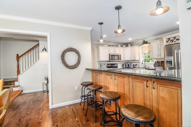 kitchen with appliances with stainless steel finishes, crown molding, a sink, dark wood finished floors, and a breakfast bar