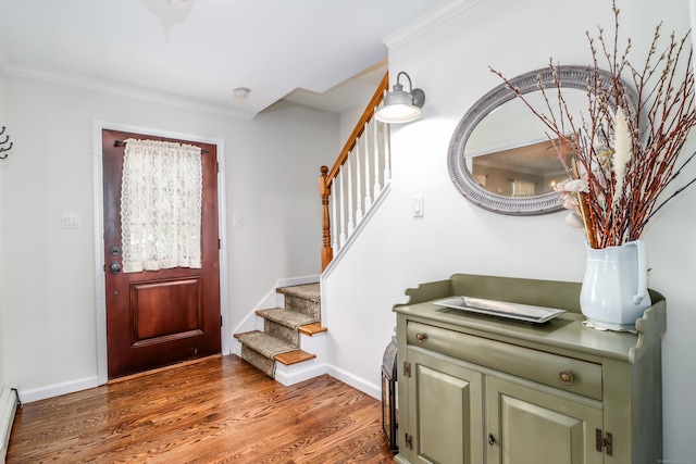 entryway with stairway, a baseboard radiator, wood finished floors, baseboards, and ornamental molding