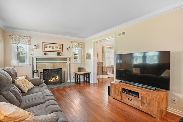 living area featuring ornamental molding, healthy amount of natural light, wood-type flooring, and a tile fireplace