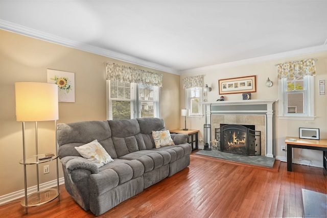 living room featuring wood-type flooring, ornamental molding, a tile fireplace, and plenty of natural light