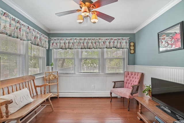 sitting room featuring a wainscoted wall, baseboard heating, crown molding, wood finished floors, and a ceiling fan