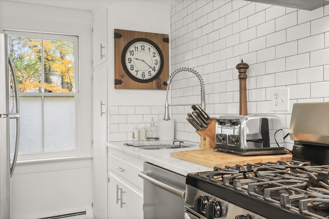 kitchen with stainless steel appliances, decorative backsplash, baseboard heating, white cabinetry, and light stone counters