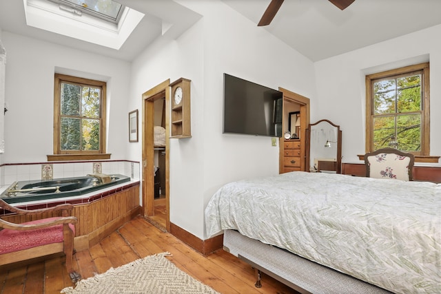 bedroom with light wood-style flooring, multiple windows, a skylight, and baseboards